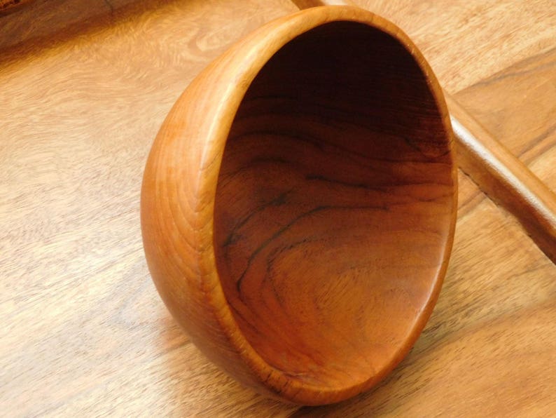May include: A large, wooden bowl with a smooth, rounded interior. The bowl is made of light brown wood with a rich grain pattern.