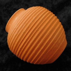 Könnte beinhalten: Ein Terrakotta-Topf mit geripptem Design. Der Topf ist hellorange und hat eine abgerundete Form.