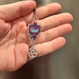 May include: A clear acrylic charm featuring a cartoon character with a television screen head, red and pink accents, and a silver pentagram charm. The charm is attached to a black cord.