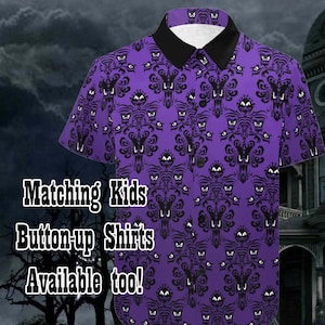 May include: Purple button-up shirt with a black collar and a repeating pattern of a haunted mansion with ghost faces. The text "Matching Kids Button-up Shirts Available too!" is printed on the shirt.