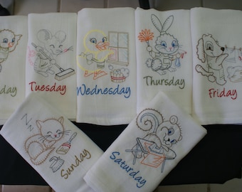 May include: Set of seven embroidered tea towels featuring a different animal and day of the week. Each towel has a white background with colorful embroidery. The animals include a bird, mouse, duck, rabbit, dog, squirrel, and cat. The days of the week are embroidered in a colorful font.