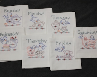 May include: Set of seven white tea towels with blue embroidered birds and teapots. Each towel features a different day of the week, including Sunday, Monday, Tuesday, Wednesday, Thursday, Friday, and Saturday.