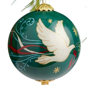 May include: A green glass Christmas ornament with a white dove carrying a sprig of holly. The dove is flying through a swirl of red and white ribbons. The ornament has a gold top and bottom.