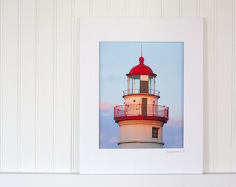 May include: A white lighthouse with a red roof and a red railing. The lighthouse is against a blue sky with some clouds.