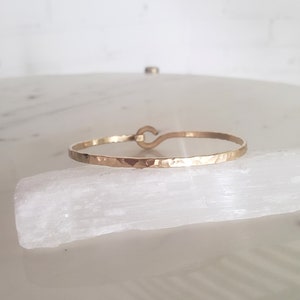 May include: A gold hammered bangle bracelet with a hook clasp.
