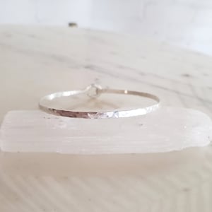 May include: A silver hammered bangle bracelet with a simple, minimalist design.