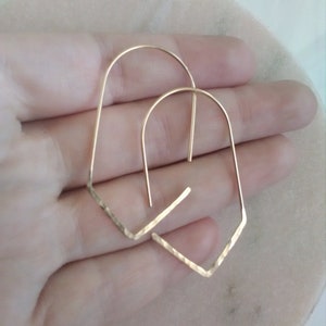 May include: A pair of gold-toned geometric hoop earrings with a hammered finish. The earrings are shaped like an upside-down V.