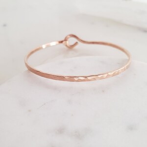 May include: A hammered rose gold bangle bracelet with a simple, open loop closure.