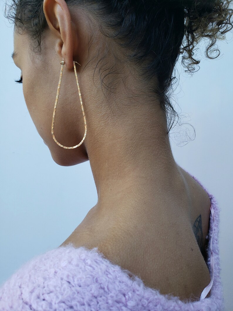 Puede incluir: Una persona con un su&eacute;ter de color morado claro y peludo con un arete de aro de oro en forma de l&aacute;grima en la oreja izquierda.