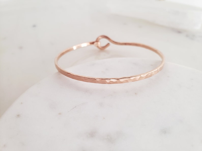 May include: A hammered rose gold bangle bracelet with a simple, open loop closure.
