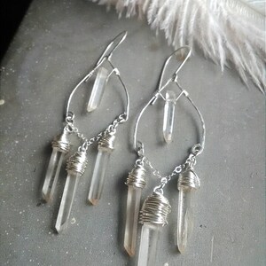 May include: Silver earrings with clear quartz crystals dangling from a wire frame. The crystals are wrapped in silver wire.