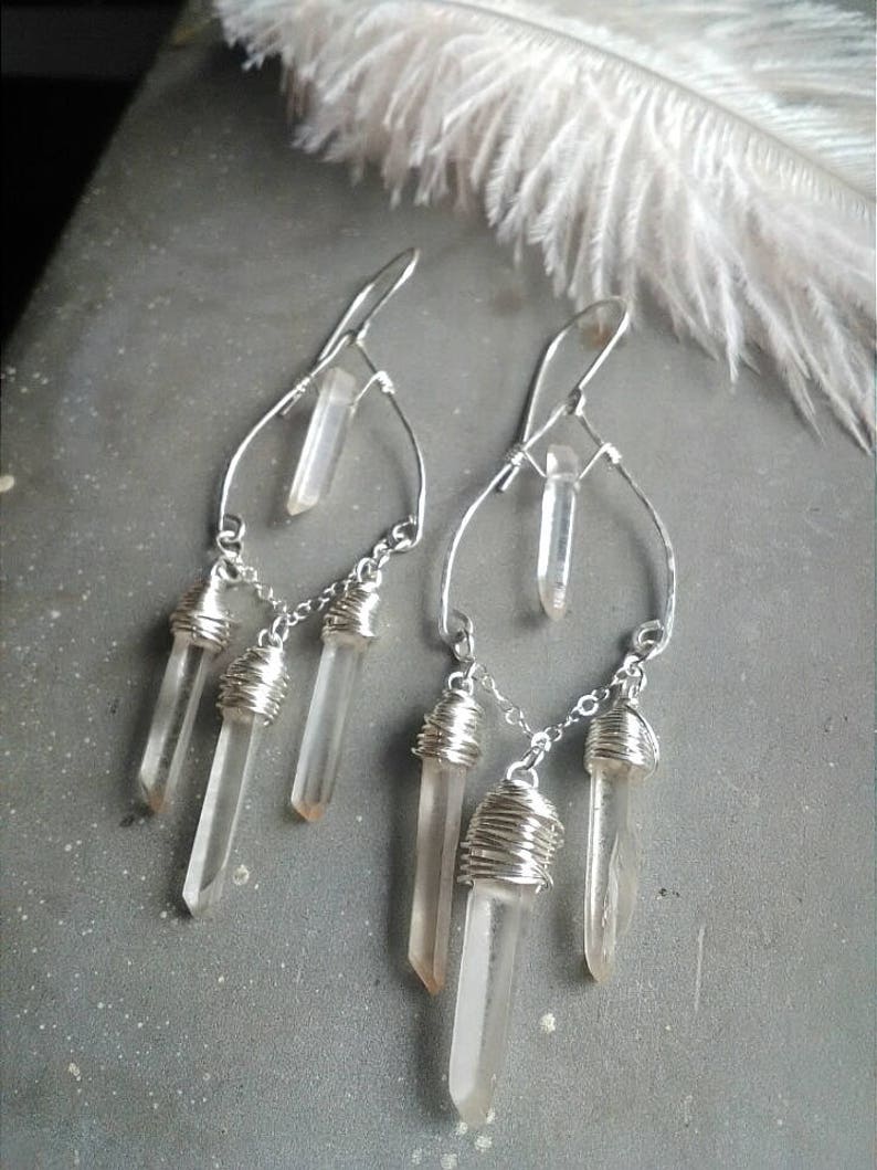 May include: Silver earrings with clear quartz crystals dangling from a wire frame. The crystals are wrapped in silver wire.