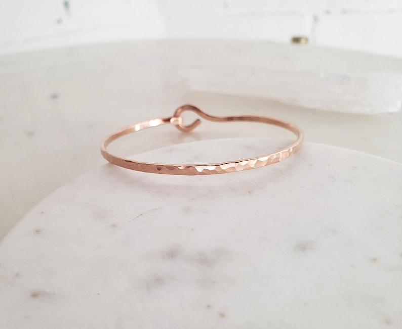 May include: A hammered rose gold bangle bracelet with a simple, open-loop design.