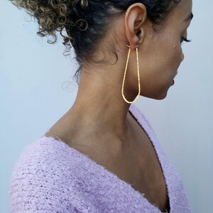 Puede incluir: Un par de pendientes de oro en forma de l&aacute;grima con textura martillada. Los pendientes son usados por una persona con cabello rizado.