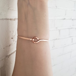May include: A rose gold bracelet with a simple, hammered knot design. The bracelet is thin and delicate, and it would make a great gift for a friend or loved one.