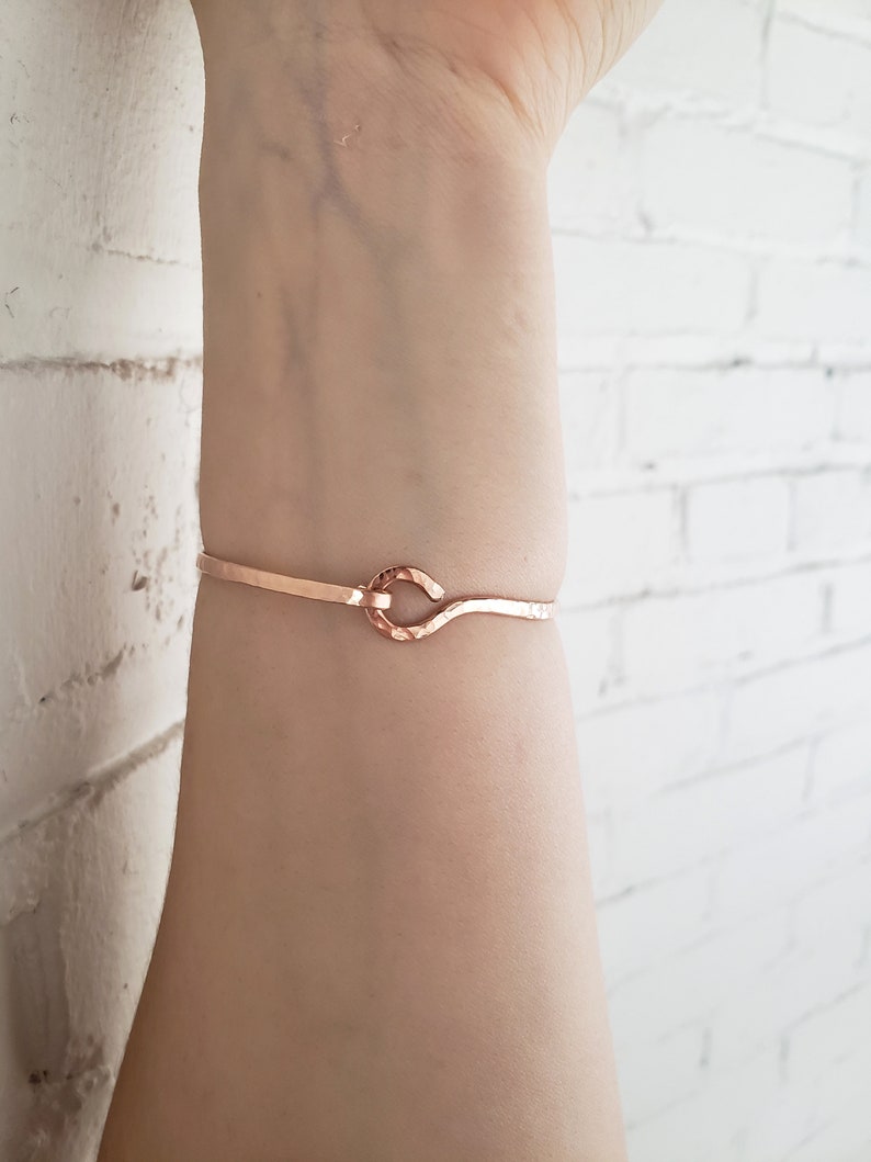 May include: A rose gold bracelet with a simple, hammered knot design. The bracelet is thin and delicate, and it would make a great gift for a friend or loved one.