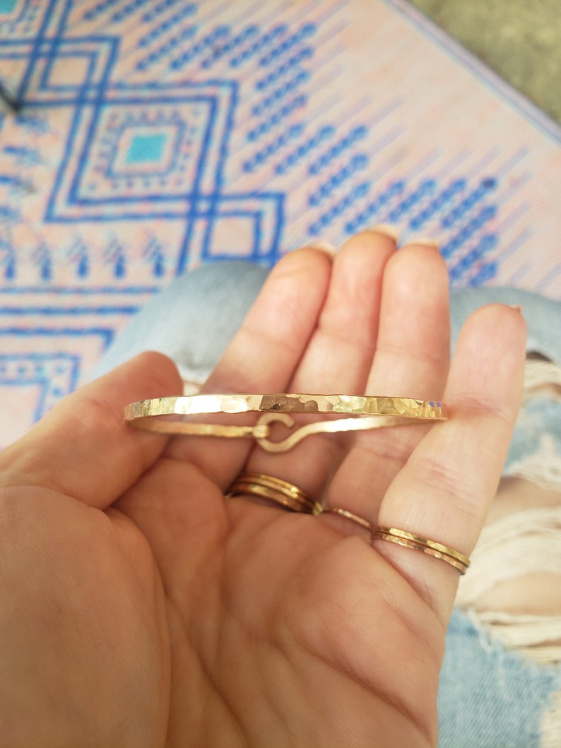 May include: A gold hammered bangle bracelet with a simple, minimalist design. The bracelet is made of a thick, durable metal and has a smooth, polished finish.