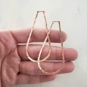 Puede incluir: Un par de pendientes de aro de oro martillados. Los pendientes son de forma ovalada y tienen un acabado texturizado.