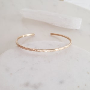 May include: A delicate gold hammered bangle bracelet. The bracelet is thin and has a smooth, hammered finish.
