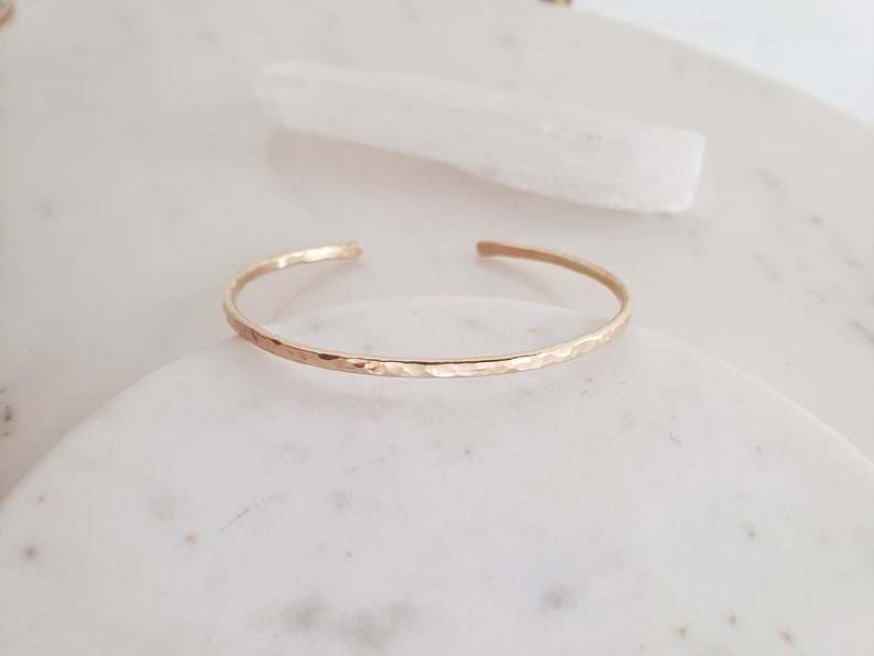 May include: A delicate gold hammered bangle bracelet. The bracelet is thin and has a smooth, hammered finish.