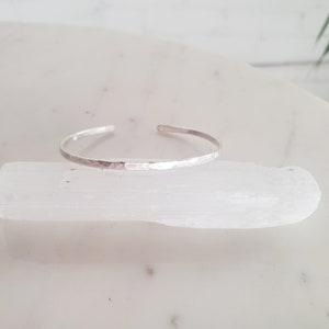 May include: A silver hammered bangle bracelet. The bracelet is thin and delicate, with a smooth, polished finish.
