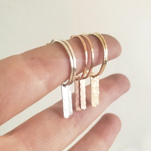 Puede incluir: Tres pendientes de aro de oro martillados con un colgante de barra. Los aros son de plata, oro rosa y oro amarillo.