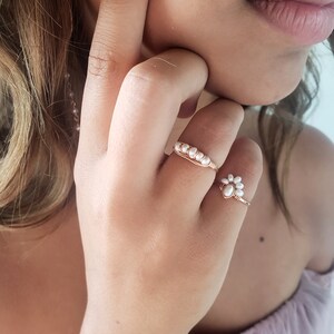 Peut inclure: Deux anneaux d&eacute;licats en or avec des accents de perles blanches. L'anneau de gauche a une rang&eacute;e de perles, tandis que l'anneau de droite a un groupe de perles en forme de fleur.