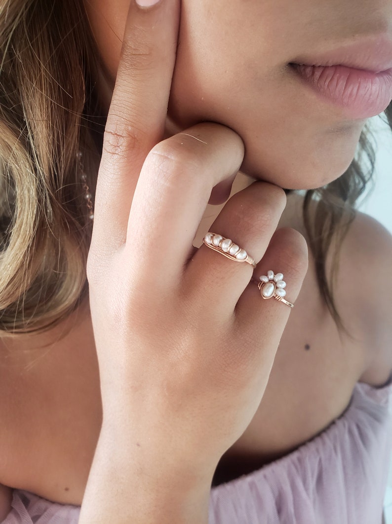 Peut inclure: Deux anneaux d&eacute;licats en or avec des accents de perles blanches. L'anneau de gauche a une rang&eacute;e de perles, tandis que l'anneau de droite a un groupe de perles en forme de fleur.
