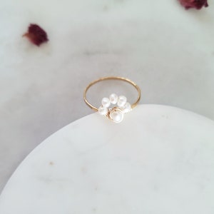 Peut inclure: Une bague en or avec un groupe de petites perles blanches et une perle plus grosse au centre.