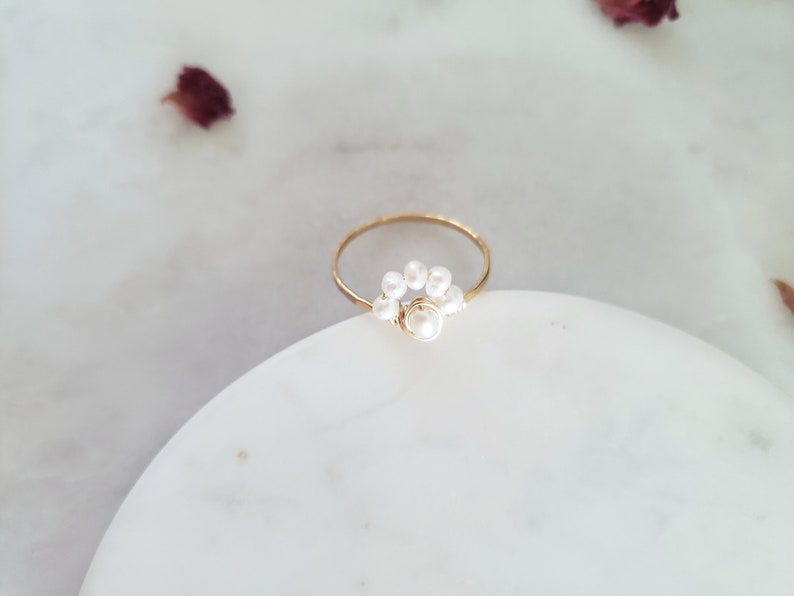 Peut inclure: Une bague en or avec un groupe de petites perles blanches et une perle plus grosse au centre.