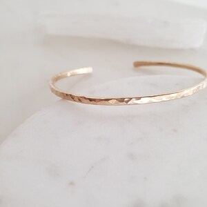 May include: A thin gold hammered bangle bracelet. The bracelet is simple and delicate, with a smooth, hammered finish.