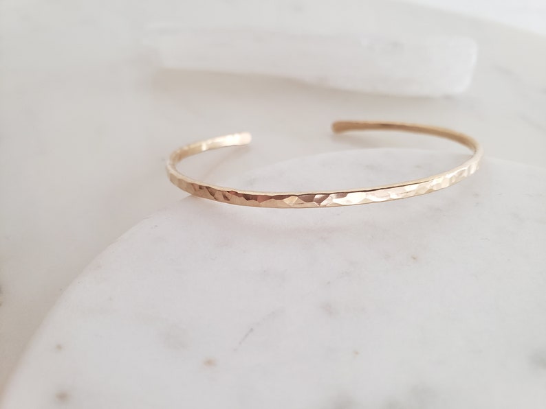 May include: A thin gold hammered bangle bracelet. The bracelet is simple and delicate, with a smooth, hammered finish.