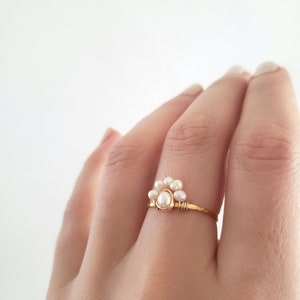 Peut inclure: Une d&eacute;licate bague en or avec un groupe de petites perles blanches. La bague est simple et &eacute;l&eacute;gante, parfaite pour tous les jours.