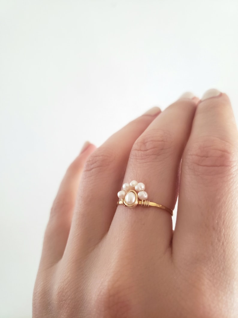 Peut inclure: Une d&eacute;licate bague en or avec un groupe de petites perles blanches. La bague est simple et &eacute;l&eacute;gante, parfaite pour tous les jours.