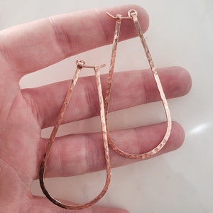 Puede incluir: Un par de pendientes de aro de l&aacute;grima de oro rosa martillados. Los pendientes est&aacute;n hechos de alambre de calibre grueso y tienen un acabado martillado.