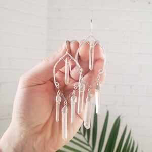 May include: Silver wire earrings with clear quartz crystal drops. The earrings feature a geometric design with multiple crystal drops hanging from a chain.