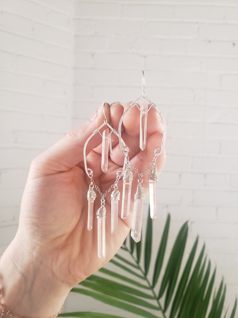 May include: Silver wire earrings with clear quartz crystal drops. The earrings feature a geometric design with multiple crystal drops hanging from a chain.