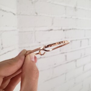 May include: A hammered rose gold bangle bracelet. The bracelet is thin and has a simple design.