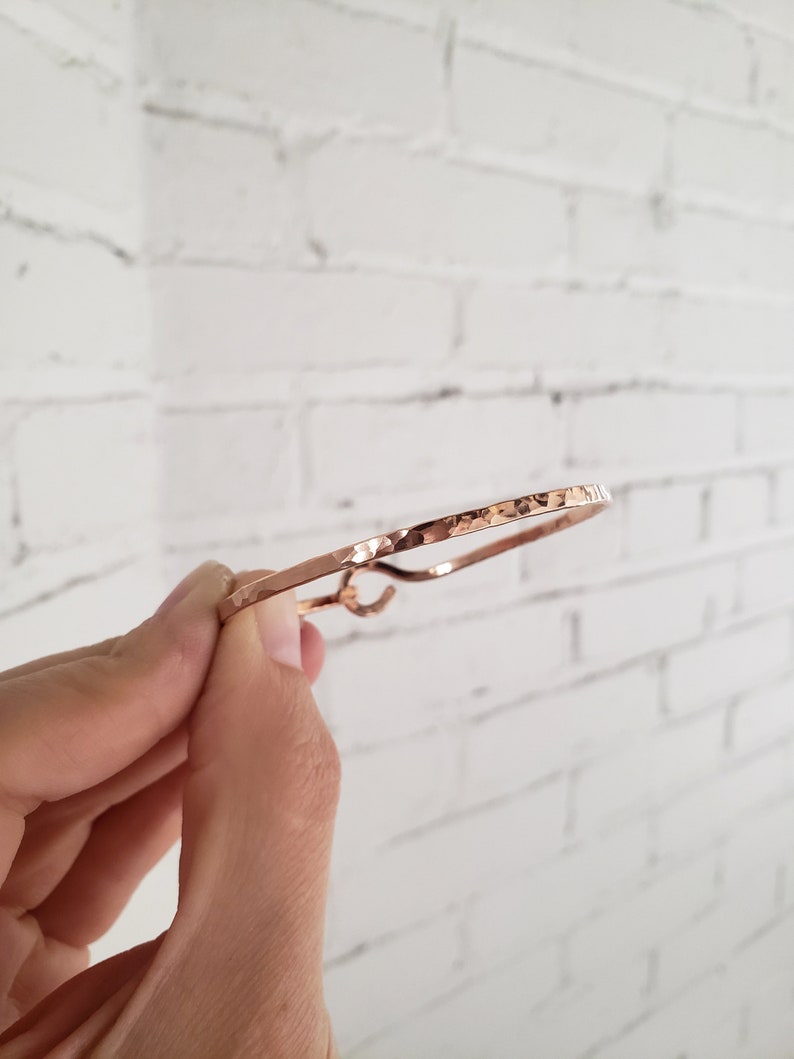 May include: A hammered rose gold bangle bracelet. The bracelet is thin and has a simple design.