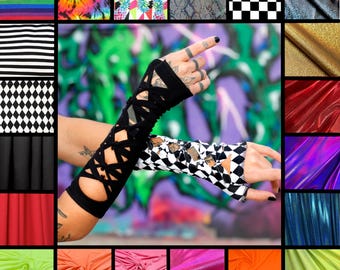 May include: A pair of arm warmers featuring a black solid fabric on one side and a black and white checkered pattern on the other. Both sleeves have a crisscross lace-up design with cutouts extending from the wrist to the forearm area.