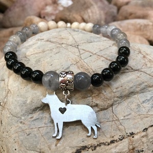 May include: A gray, white, and black beaded bracelet with a silver charm of a dog silhouette. The charm has a small heart cutout.