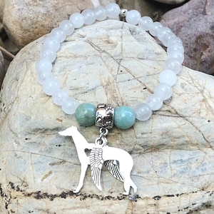 May include: A white beaded bracelet with a silver charm featuring a Greyhound dog with angel wings. The bracelet includes two turquoise beads and a silver spacer with paw prints.