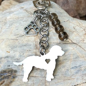 May include: Silver-toned keychain featuring a dog silhouette with a heart cutout, a paw print charm, and brown bead accents. The keychain has a clasp for easy attachment and is designed for pet lovers.