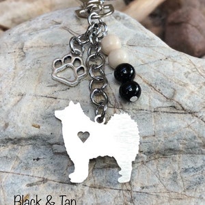 May include: A silver keychain featuring a silhouette of a dog with a heart cutout, a paw print charm, and black and white beads. The text "Black & Tan" is visible at the bottom of the image.