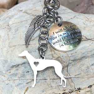 May include: A silver-colored keychain featuring a Greyhound dog silhouette with a heart cutout, a wing charm, and a circular tag with the inscription "I will hold you in my heart until I hold you in heaven."