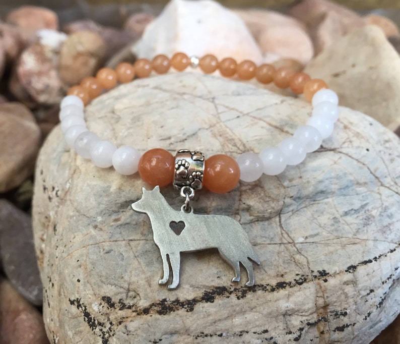 May include: A white and orange beaded bracelet with a silver dog charm. The charm has a heart cut out of it.