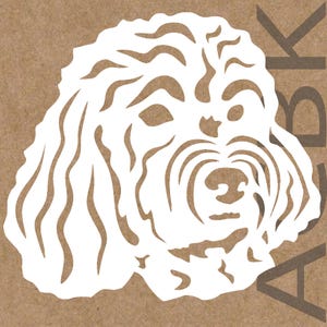Op de afbeelding: Een witte papieren uitsnede van een hondengezicht, met gedetailleerde vacht en gelaatstrekken. De kop van de hond is gecentreerd, met de letters "ABK" zichtbaar op de achtergrond. De afbeelding staat tegen een bruine achtergrond.