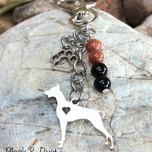 May include: Silver keychain featuring a Doberman silhouette with a heart cutout, a paw print charm, and brown and black beads. "Black & Rust" is written on the bottom.