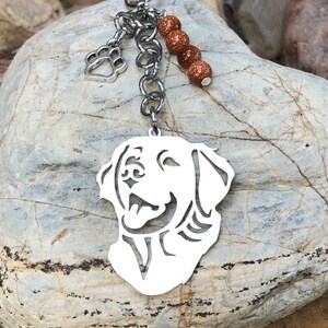 May include: Silver keychain featuring a cutout silhouette of a golden retriever dog's head. The keychain has a silver paw print charm and a chain with brown glitter beads.