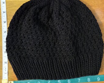 May include: A black knitted beanie hat. The hat is made of a dark yarn and has a ribbed brim. The hat measures approximately 9 inches across.